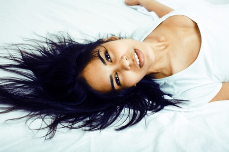 young pretty tann woman in bed among white sheets having fun, trying to sleep, fooling aroundの写真素材