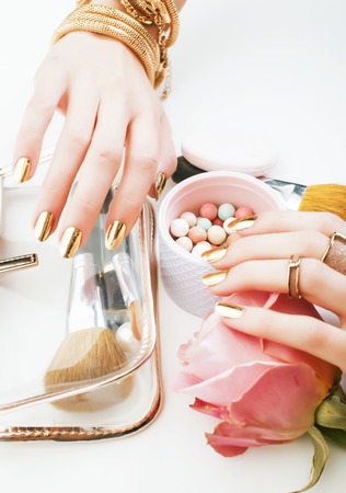 woman hands with golden manicure and many rings holding brushes, makeup artist stuff stylish, pure close up pink flower rose among cosmetic for makeupの写真素材