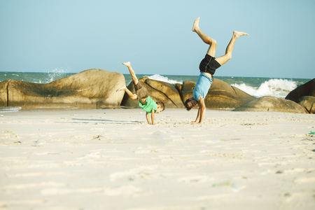 happy family on beach playing, father with son walking sea coast, rocks behind smiling taking vacationの写真素材