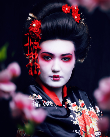 young pretty geisha in kimono with sakura and decoration on black backgroundの写真素材