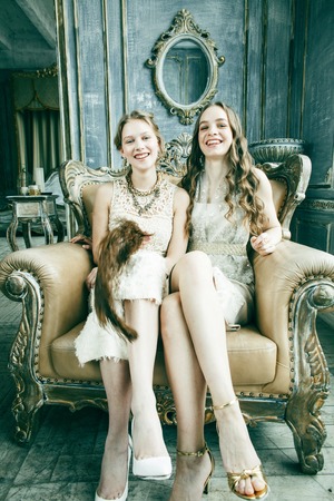 two pretty twin sister blond curly hairstyle girl in luxury house interior together, rich young people conceptの写真素材