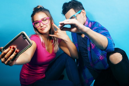 happy couple together posing cheerful on blue background wearing glasses, guy and girl students together friendsの写真素材
