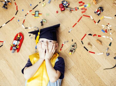 little cute preschooler boy playing toys at home happy smiling in graduation hat, lifestyle children , world map with pieces, self education conceptの写真素材