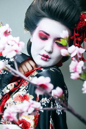 young pretty geisha in black kimono among sakura, asian ethno closeupの写真素材