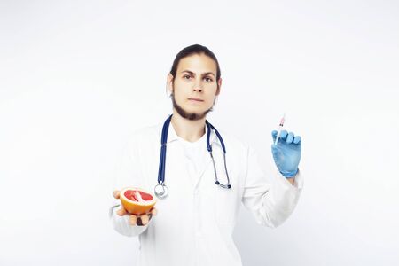 young pretty doctor with stethoscope holding fruits, vegetables and pills, syringe, healthy food care conceptの写真素材
