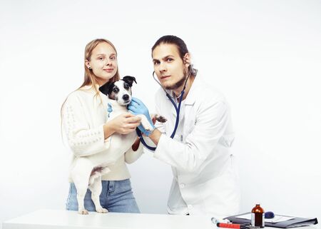 young veterinarian doctor in blue gloves examine little cute dog jack russell isolated on white background with owner blond girl holding it, animal healthcareの写真素材