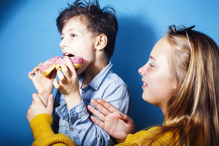 happy family brother and sister eating donuts on blue background, lifestyle people concept, boy and girl eating unhealthy foodの写真素材