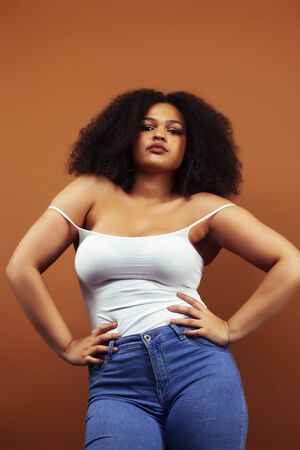 pretty young african american woman with curly hair posing cheerful gesturing on brown background, lifestyle people conceptの写真素材
