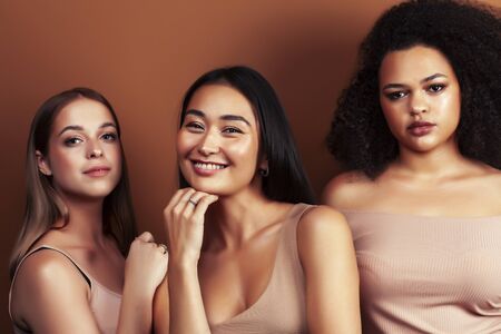 young pretty asian, caucasian, afro woman posing cheerful together on brown background, lifestyle diverse nationality people conceptの写真素材