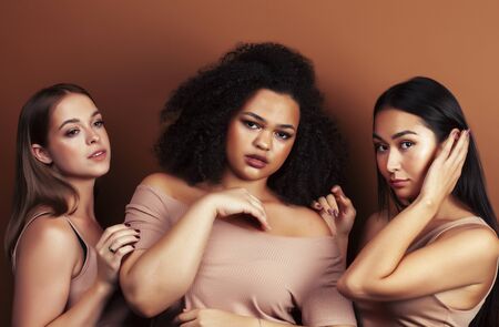 young pretty asian, caucasian, afro woman posing cheerful together on brown background, lifestyle diverse nationality people conceptの写真素材