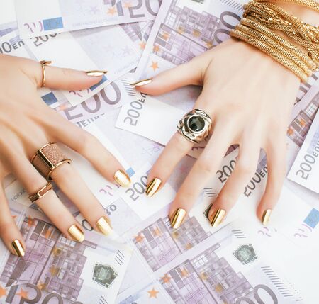 hands of rich woman with golden manicure and many jewelry rings on cash euros close upの写真素材