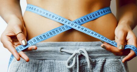 woman measuring waist with tape on knot like a gift closeup on white backgroundの写真素材
