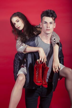 young pretty guy and girl closed in fashion style after party shoes in hand posing on red background, lifestyle people conceptの写真素材