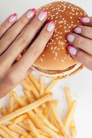 woman hand with manicure holding big burger french fries on background, people eating food concept closeupの写真素材