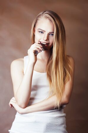 young cute blond girl eating chocolate and smiling on brown background, lifestyle people conceptの写真素材
