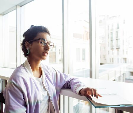 young cute indian girl at university building sitting on stairs reading a book, wearing hipster glasses, lifestyle people concept close upの写真素材
