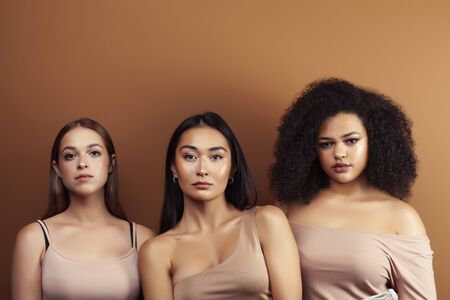 young pretty asian, caucasian, afro woman posing cheerful together on brown background, lifestyle diverse nationality people conceptの写真素材