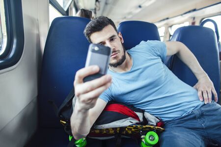 young pretty modern hipster guy traveller on train with skateboard alone, lifestyle vacation people...