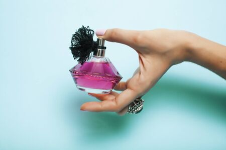 woman hands holding bottle of perfume pink manicure and jewelry on blue background, cosmetic care...