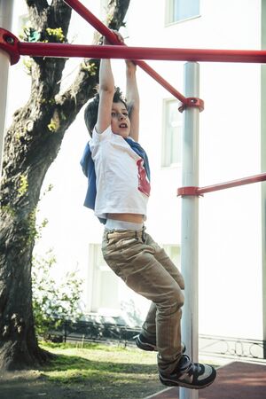 little cute blond boy hanging on playground outside, alone training with fun, lifestyle children...