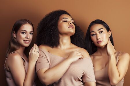 young pretty asian, caucasian, afro woman posing cheerful together on brown background, lifestyle diverse nationality people conceptの写真素材