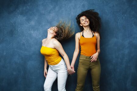 young pretty teenage girls friends with blond and brunette curly hair posing cheerful on blue background, lifestyle people conceptの写真素材