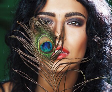 young sensitive brunette woman with peacock feather eyes closeup on green smiling, lifestyle people...