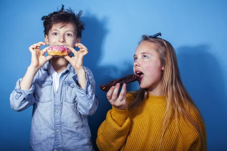 happy family brother and sister eating donuts on blue background, lifestyle people concept, boy and girl eating unhealthy foodの写真素材