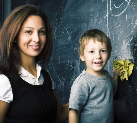 little cute boy in glasses with young real teacher, classroom studying at blackboard school kido