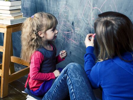 young teacher with little gitl pupil painting on blackboard, self education mother with daughter...