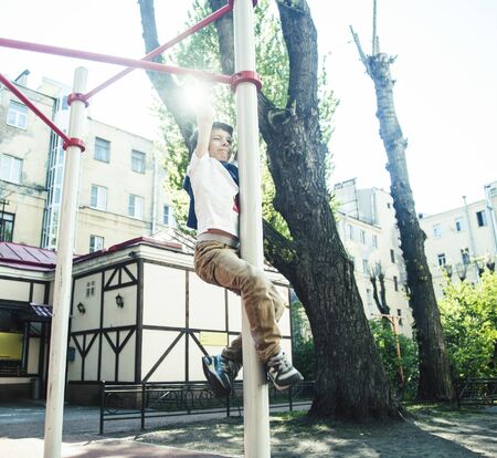 little cute blond boy hanging on playground outside, alone training with fun, lifestyle children...