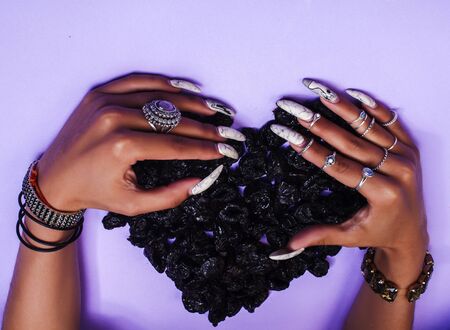 woman hands with long nails manicure holding dry fruits in shape of heart on purple background