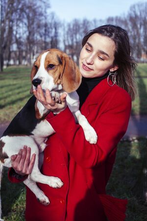 pretty young girl in redd coat playing with dog outside in green park, lifestyle people conceptの写真素材