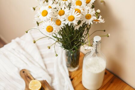 Simply stylish wooden kitchen with bottle of milk and glass on table, summer flowers camomile, healthy foog moring conceptの写真素材