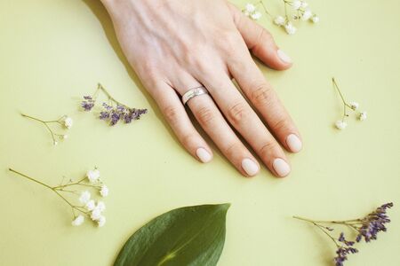 pretty perfect woman hands with white manicure and little flowers on colorful yellow background, spa conceptの写真素材