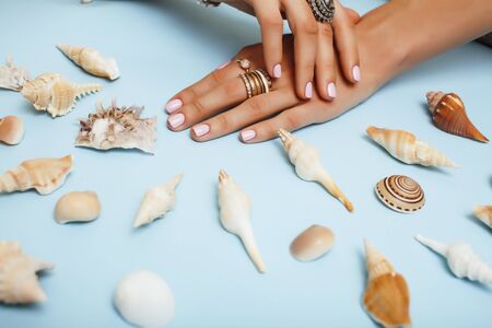 beautiful woman hands with pink manicure holding sea shells, lot of rings on fingers on blue background, luxury jewelry conceptの写真素材