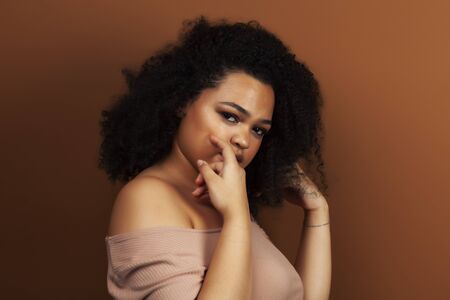 pretty young african american woman with curly hair posing cheerful gesturing on brown background,...