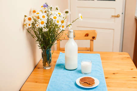 Simply stylish wooden kitchen with bottle of milk and glass on table, summer flowers camomile, healthy foog moring conceptの写真素材