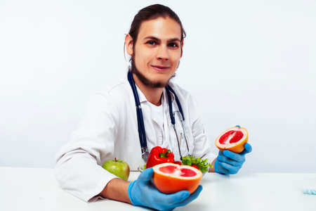 young pretty doctor with stethoscope holding fruits, healthy food care conceptの写真素材