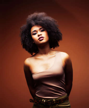 pretty young african american woman with curly hair posing cheerful gesturing on brown background, lifestyle people conceptの写真素材