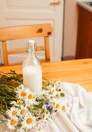 Simply stylish wooden kitchen with bottle of milk and glass on table, summer flowers camomile, healthy foog moring conceptの写真素材