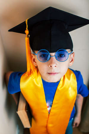 little cute preschooler boy in glasses with books at home education in graduate hat smiling posing emotional, lifestyle people conceptの写真素材
