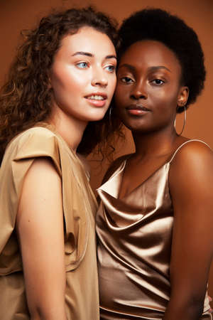 two pretty girls african and caucasian blond posing cheerful together on browm background, etnithity diverse lifestyle people conceptの写真素材