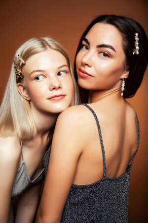 two pretty diverse girls happy posing together: blond and brunette on brown background, lifestyle people conceptの写真素材