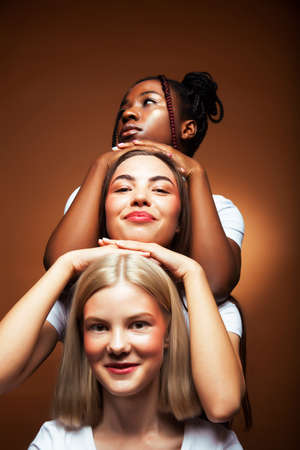 young pretty asian, caucasian, afro woman posing cheerful together on brown background, lifestyle diverse nationality people conceptの写真素材
