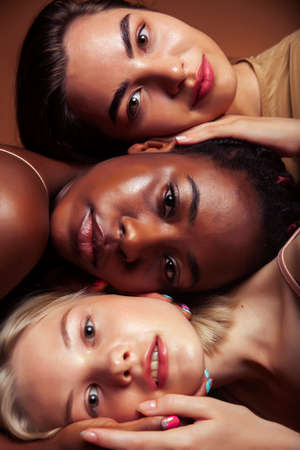 young pretty asian, caucasian, afro woman posing cheerful together on brown background, lifestyle...