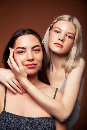 two pretty diverse girls happy posing together: blond and brunette on brown background, lifestyle people conceptの写真素材