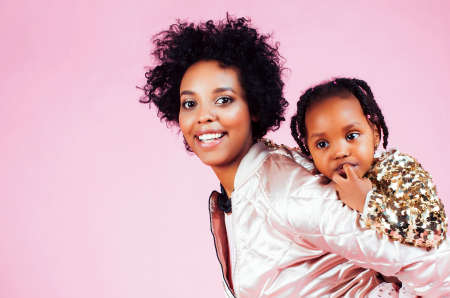 young pretty african-american mother with little cute daughter hugging, happy smiling on pink background, lifestyle modern people conceptの写真素材