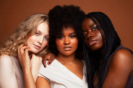 young pretty caucasian, afro, scandinavian woman posing cheerful together on brown background, lifestyle diverse nationality people conceptの写真素材
