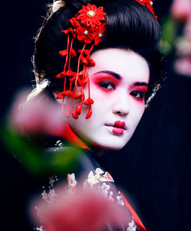 young pretty real geisha in kimono with sakura and decoration on black backgroundの写真素材